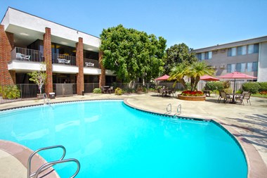 Apartments in Downey - Park Regency Club - Enclosed Pool with Lounge Chairs, Tables, and Red Umbrellas