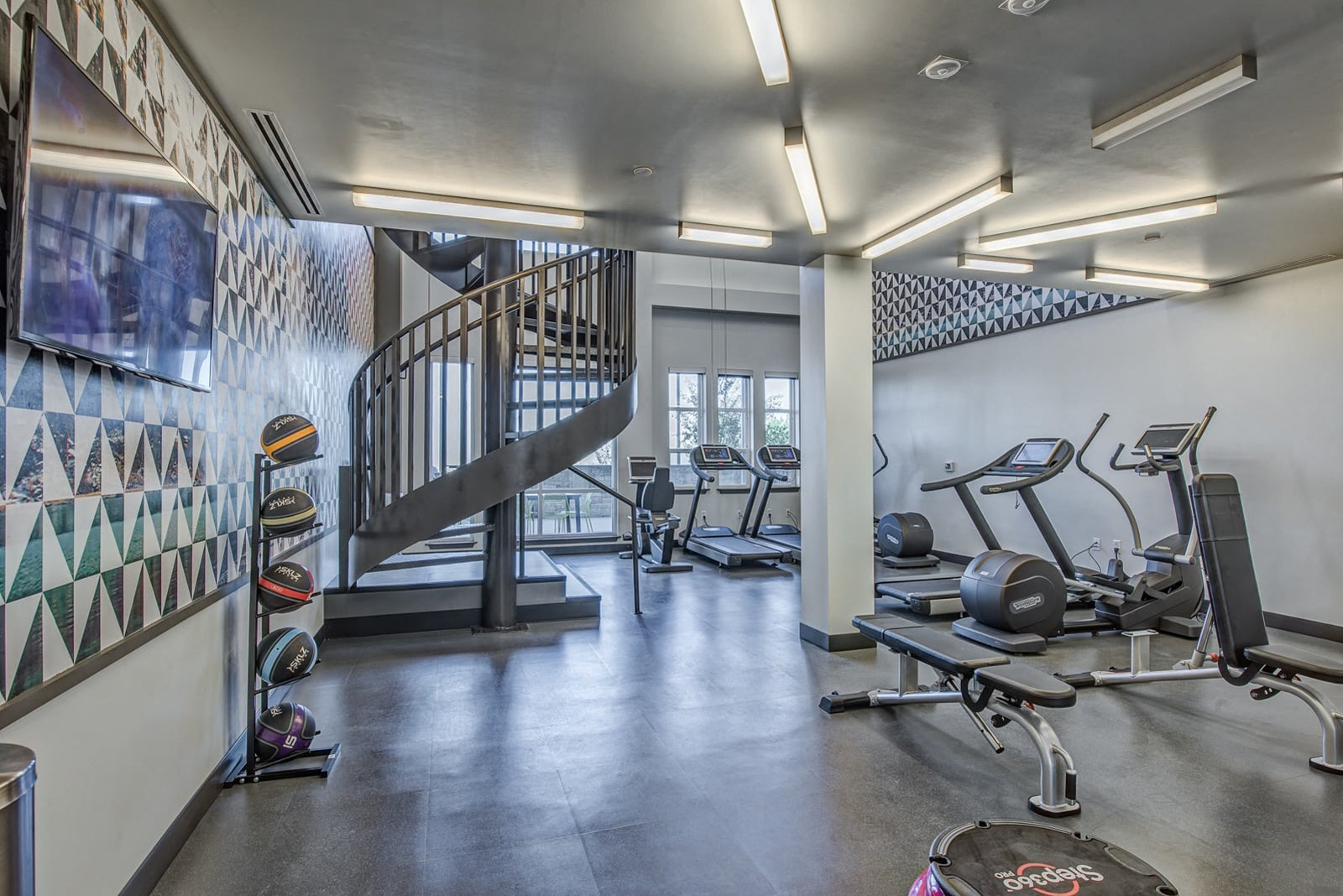 Two-story 24/7 fitness center featuring Technogym® cardio equipment with iPod connectivity, viewing screens for internet