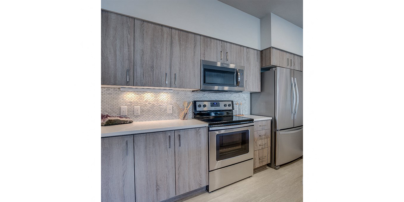 Tigard OR Apartments for Rent - Sygnii - Modern Kitchen with Wood-Style Cabinetry, White Countertops, Stainless Steel Appliances, Tile Backsplash, and Plank Flooring