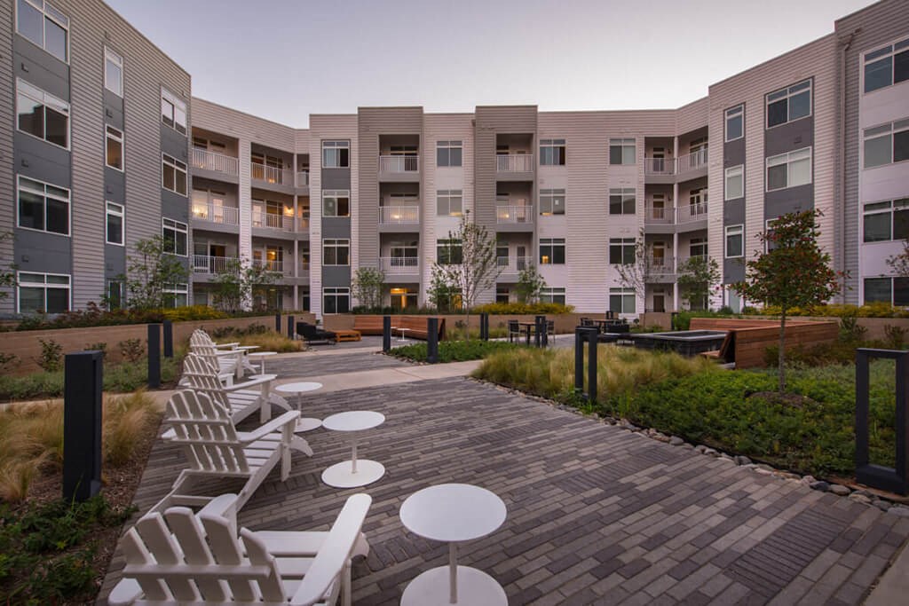 a courtyard with white chairs and tables in front of an apartment building