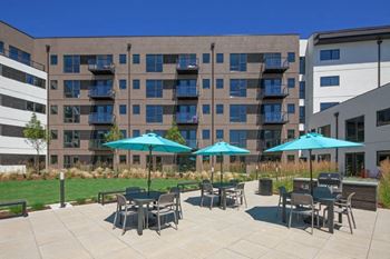 a patio with tables and umbrellas in front of an apartment building