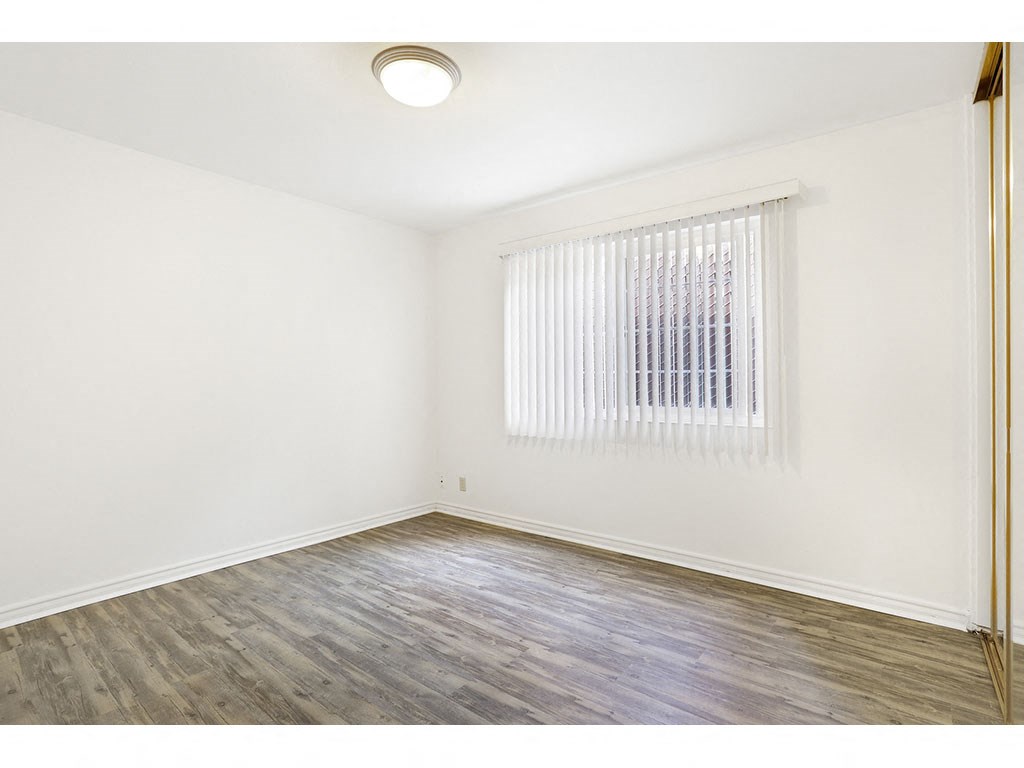 1 Bedroom Apartments in Hayward CA - Paseo Gardens - Bedroom with Wood Floors, a Window with Blinds, and a Spacious Closet with Mirrored Sliding Doors