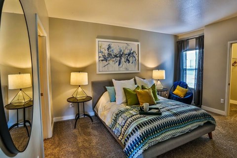 A bedroom with a bed, two lamps, and a painting on the wall.