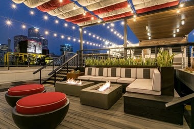 a rooftop deck with couches and fire pits and a view of the city at night
