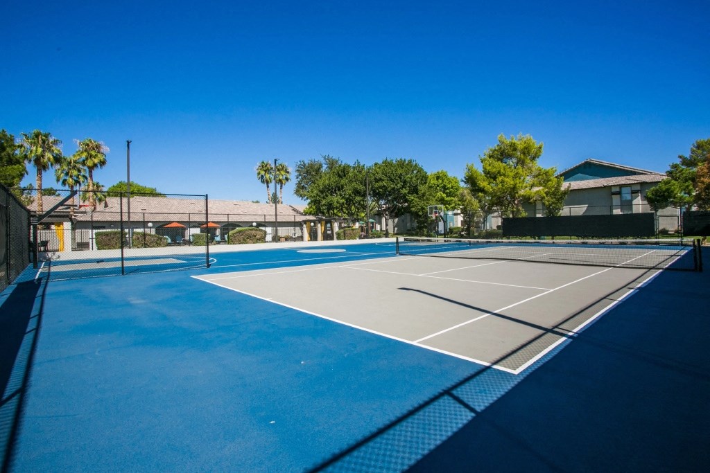 a tennis court with palm trees and a building in the background