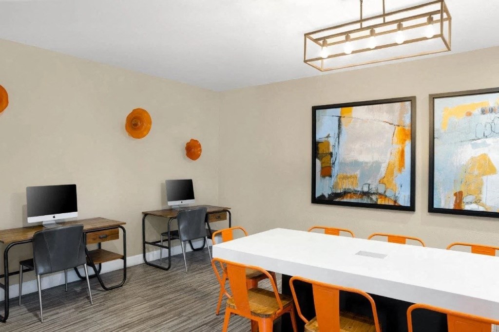 a computer room with a white table and chairs and two monitors