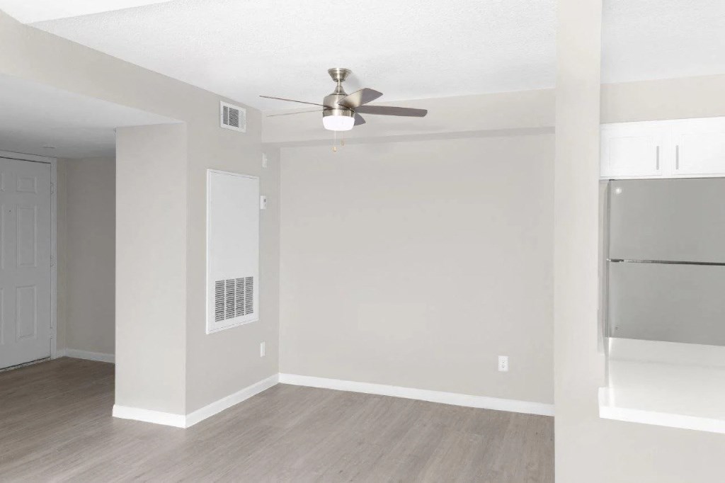 an empty living room with a ceiling fan and a refrigerator