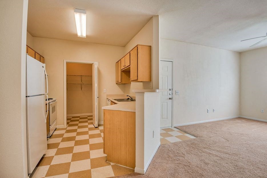 Beaumont, TX Apartments – Breakwater Bay - Kitchen with tile flooring, stainless steel sink, plenty of cabinets for storage, oven/stove top, fridge, pantry. Living room with plush carpet.