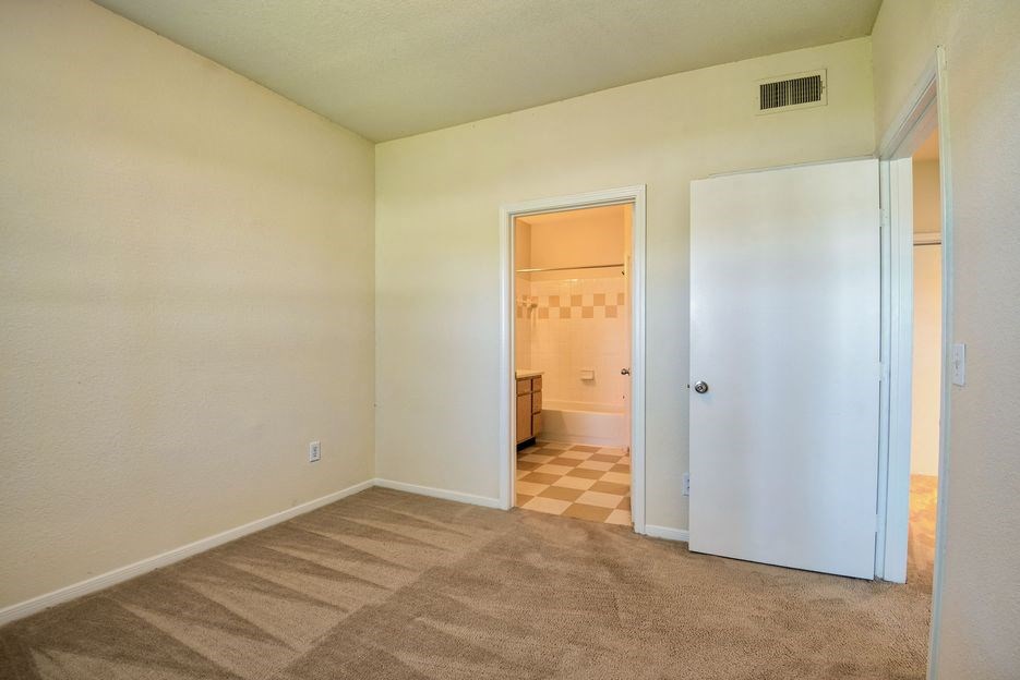 Beaumont, TX Apartments – Breakwater Bay - Bedroom with plush carpet, window with coverings and door to private bathroom