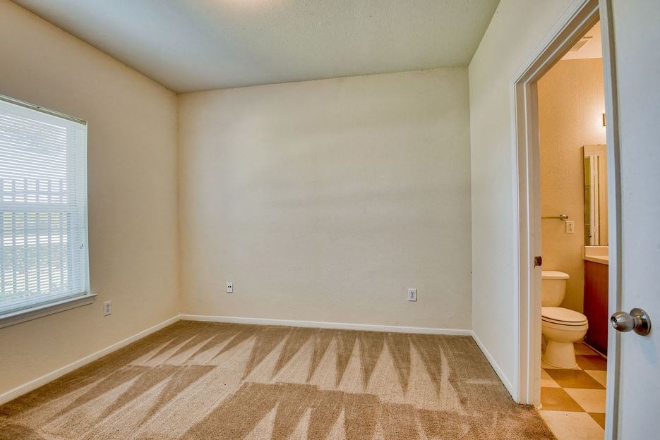 Pet-Friendly Apartments in Beaumont, TX – Breakwater Bay - Bedroom with plush carpet, window with coverings and door to private bathroom