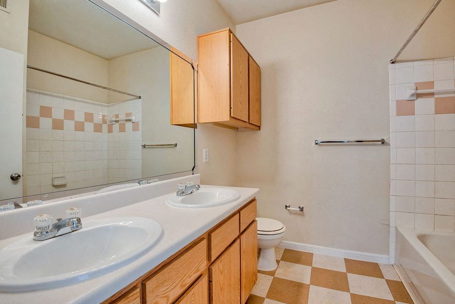 Apartments In Beaumont, TX for Rent – Breakwater Bay - Bathroom with tile flooring, double vanity, cabinets below sink, giant mirror above sink, toilet with storage above, and tub/shower