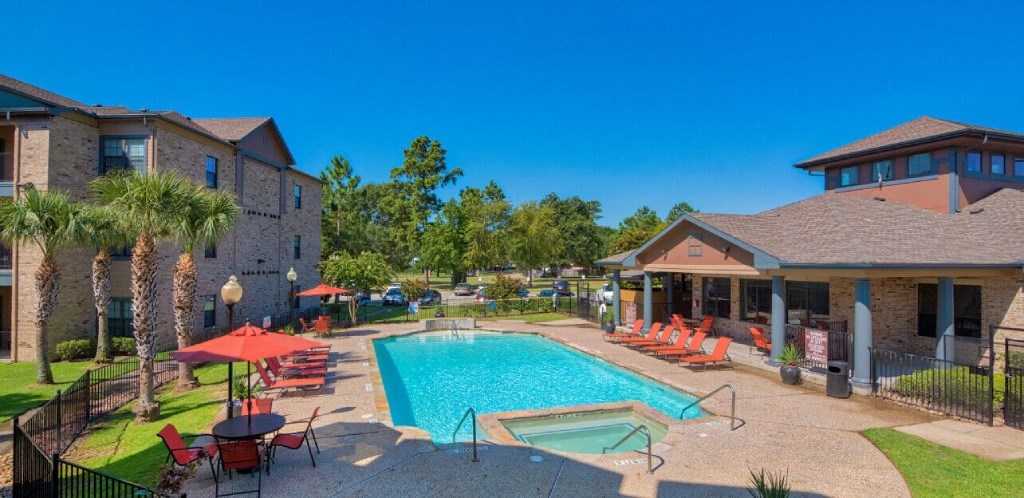 A swimming pool at Lake forest surrounded by beach umbrellas and beach chairs and trees