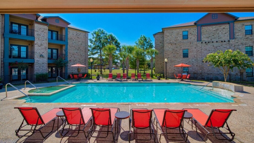 A swimming pool at Lake forest surrounded by beach umbrellas and beach chairs and trees