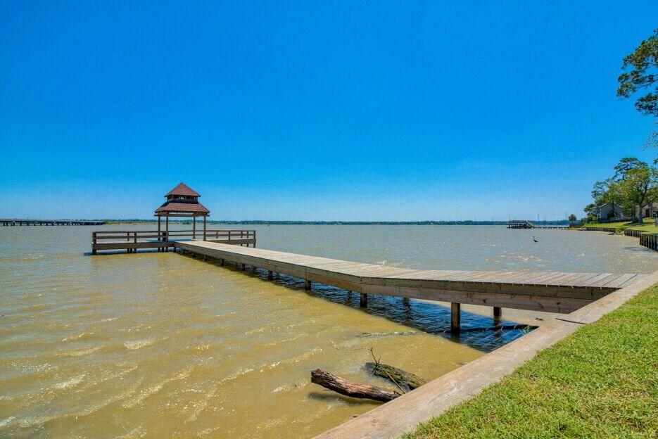 A grassy field with a dock that leads above the water on a bridge to a covering
