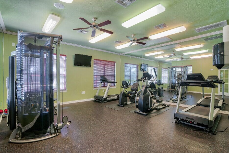 A gym with ceiling fans and cardio equipment and lifting equipment 
