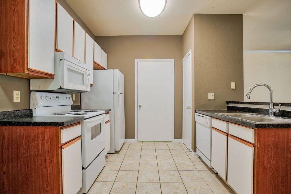 kitchen with tile floor and white cabinets and white appliances with steel sink and carpet living room
