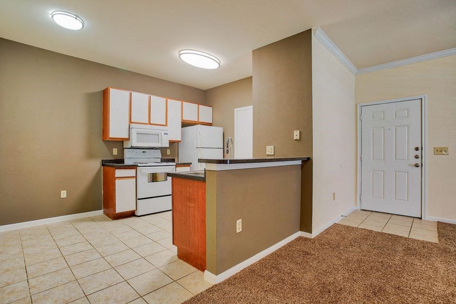 kitchen with tile floor and white cabinets and white appliances with steel sink and carpet living room