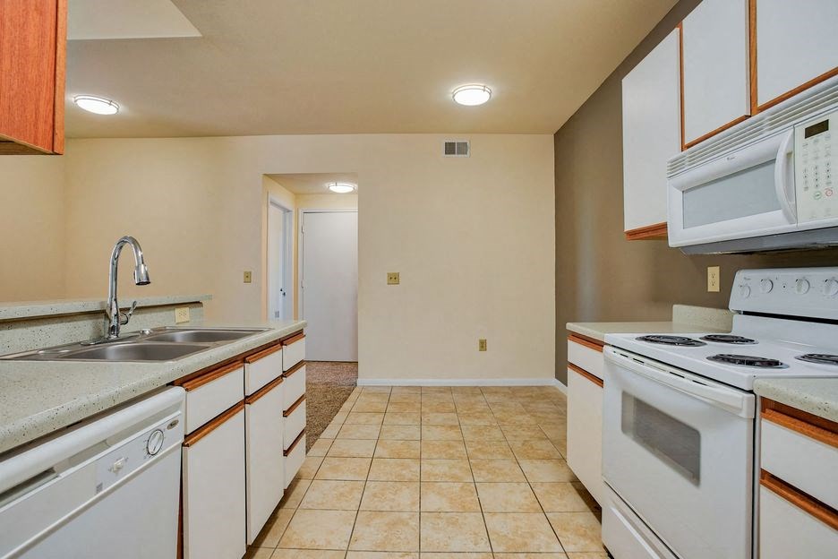 kitchen with tile floor and white cabinets and white appliances with steel sink and carpet living room