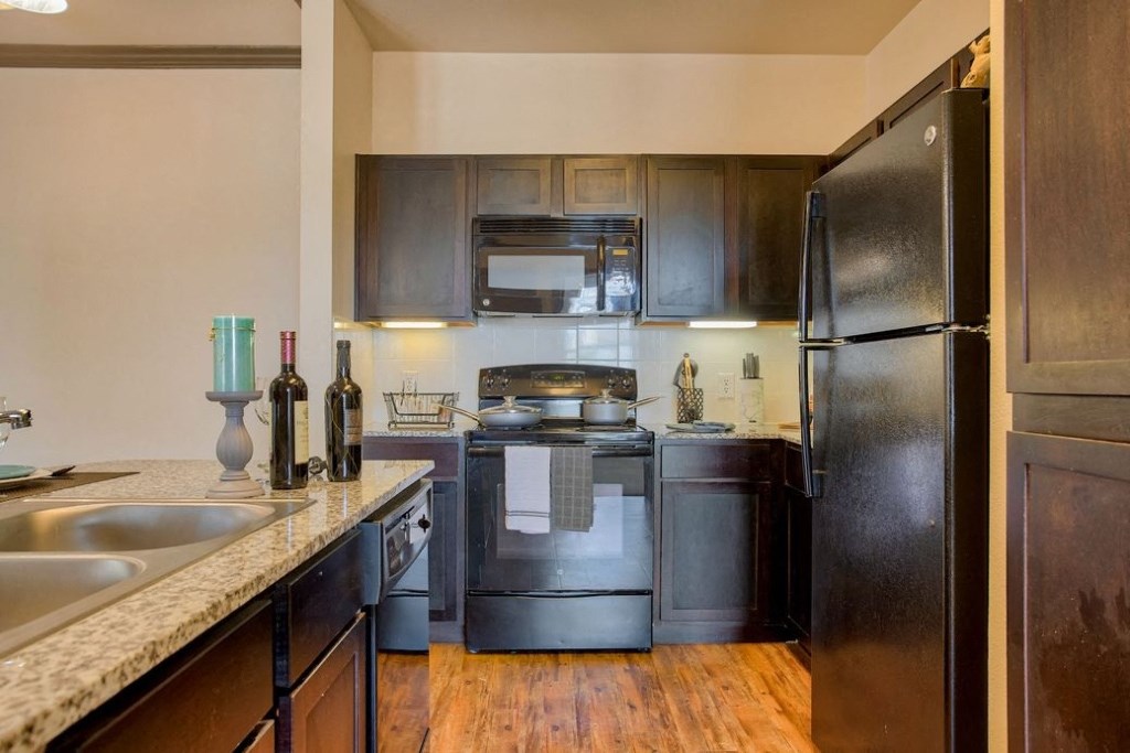 Kitchen with wood floors and black appliances and wood cabinets and stainless steel sink