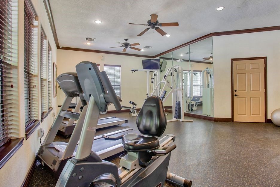 Gym with fitness and cardio equipment with a ceiling fan and windows