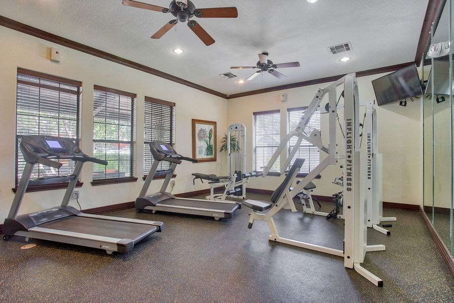 Gym with fitness and cardio equipment with a ceiling fan and windows