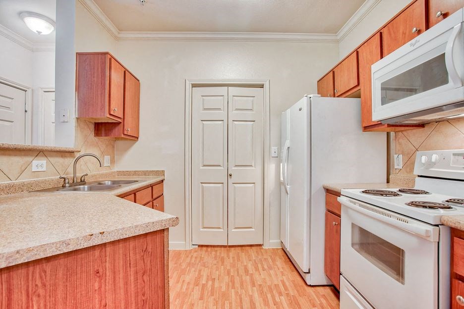Kitchen with a sink, pantry door, white fridge, white stove top/oven, white microwave and wood cabinets with a marble countertop