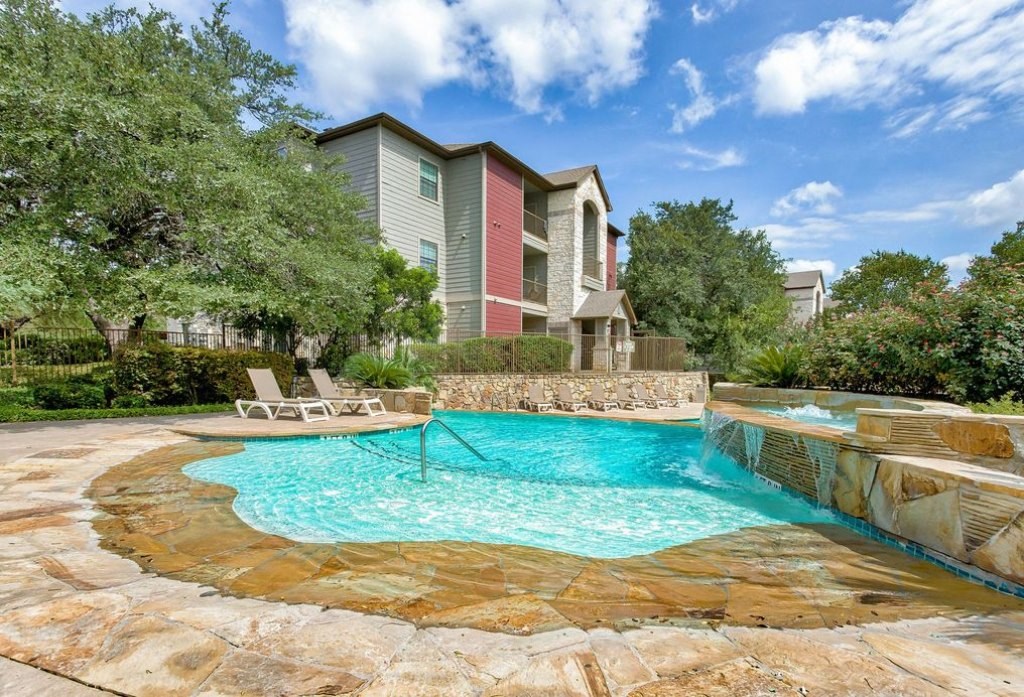 A pool surrounded by rock floors and beach chairs and apartments