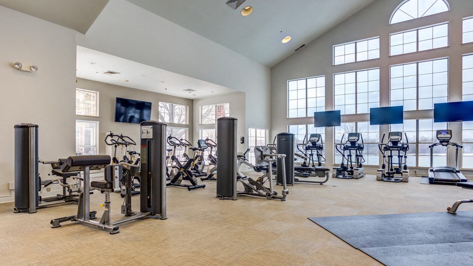 the fitness center has a large amount of exercise equipment and windows