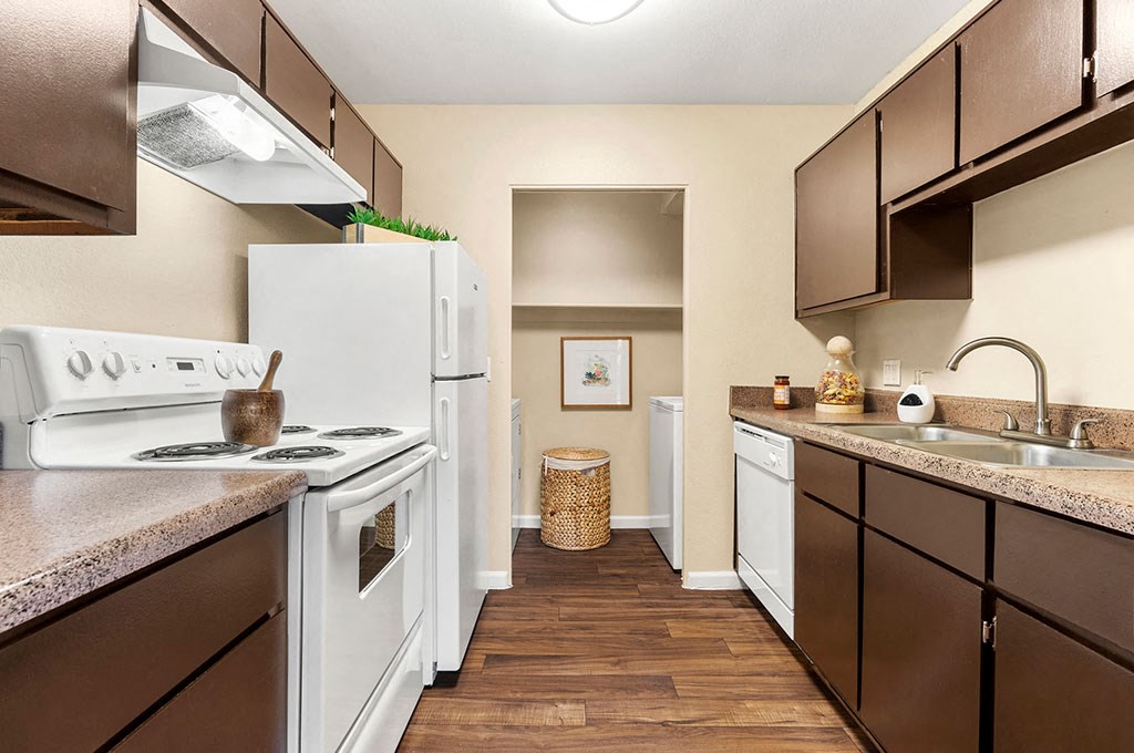North Phoenix, AZ Apartments - Cobblestone - A Kitchen With Wood-Style Flooring, White Appliances, Dark Cabinetry, And A Laundry Room At One End