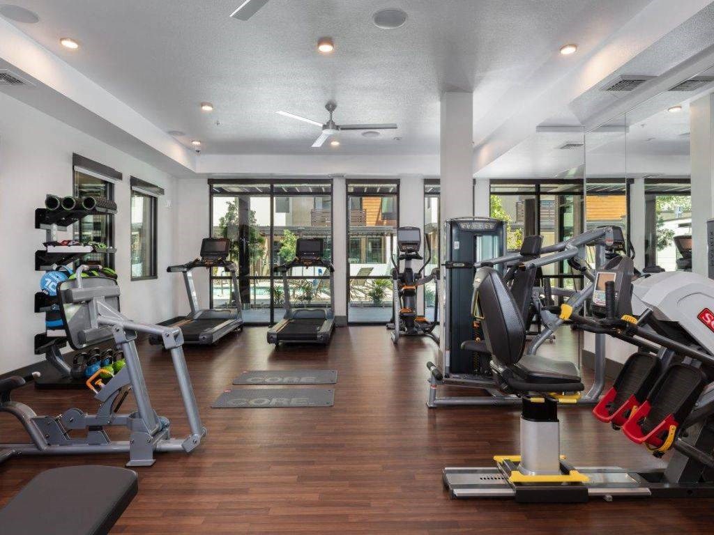Apartments for Rent in Santa Clara, CA - Santana Terrace - Fitness Center with Wood-Style Flooring, Ceiling Fans, Floor-To-Ceiling Windows, Cardio Machines, and Strength Training Machines