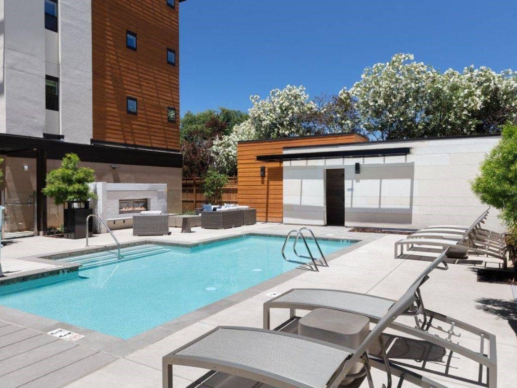 Two-Bedroom Apartments in Santa Clara, CA - Santana Terrace - Swimming Pool with a Fireplace, Lounge Seating, and Lush Landscaping