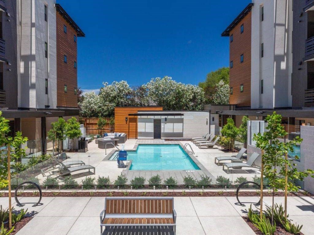 1-Bedroom Apartments in Santa Clara, CA - Santana Terrace - Swimming pool with Lounge Chairs, Beautiful Landscaping, and a Wooden Bench in Front