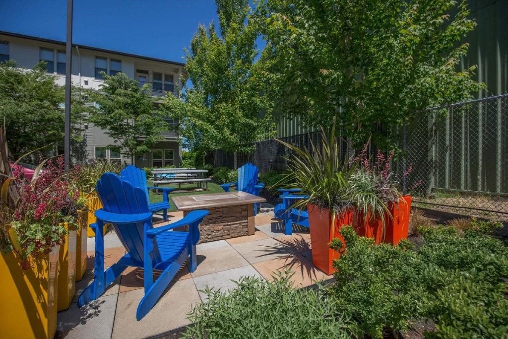 a patio with blue chairs and potted plants and a fire pit