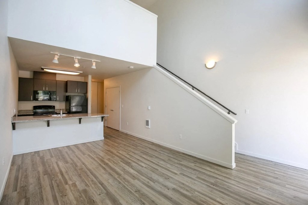 the living room and kitchen of an empty apartment with white walls and wood flooring