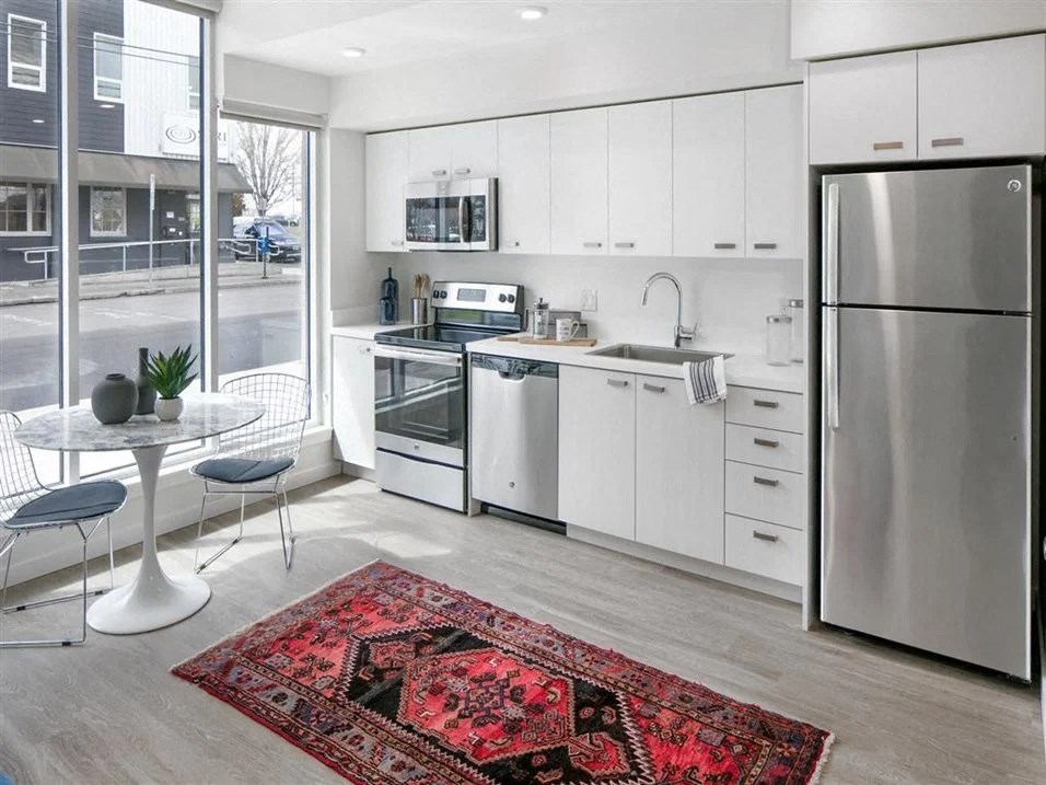Pet-Friendly Apartments In Beaverton, OR - Westline - Kitchen With Vinyl Hardwood Plank Flooring, White Cabinets, Stainless Steel Appliances, White Counters, And A Floor-To-Ceiling Window