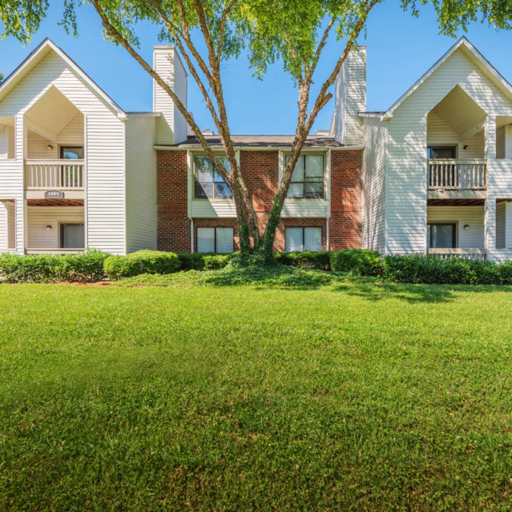 an exterior view of an apartment building with green grass and a tree