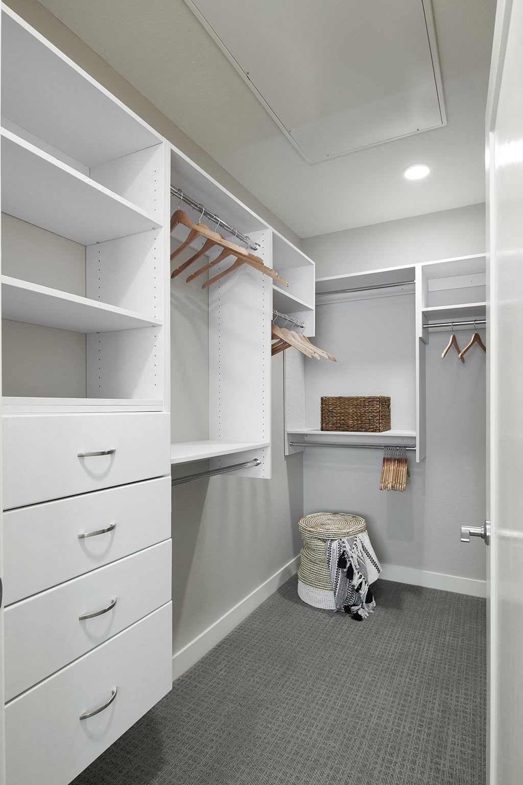a walk in closet with white cabinets and shelves and a stool