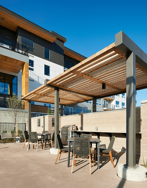 a patio with tables and chairs under a wooden canopy