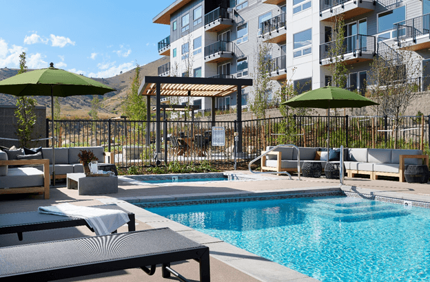 a swimming pool with chairs and umbrellas in front of an apartment building