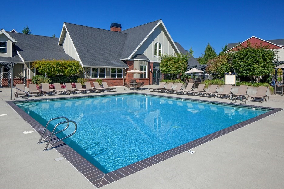 a swimming pool with chairs around it in front of a house