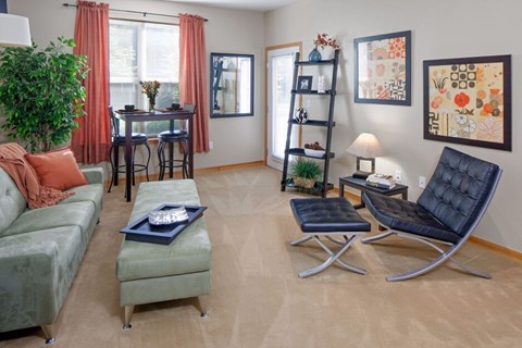 A living room with a green couch, a black chair, and a table with a vase on it.