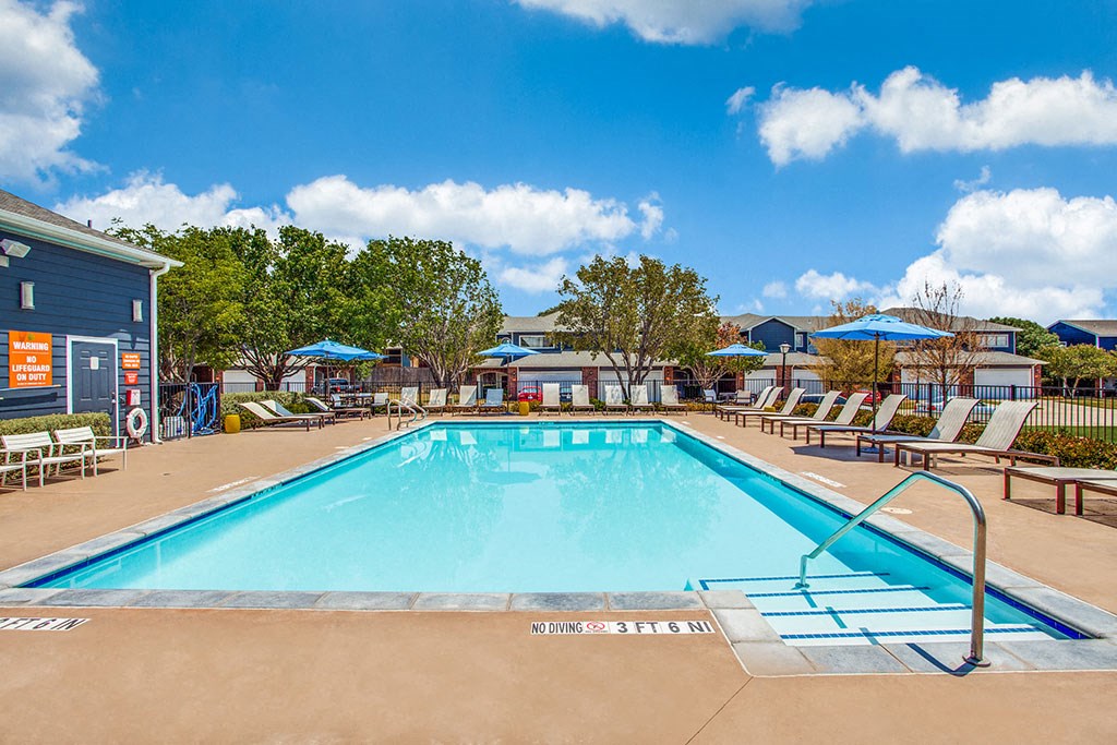 a swimming pool with chaise lounge chairs and umbrellas in front of a building