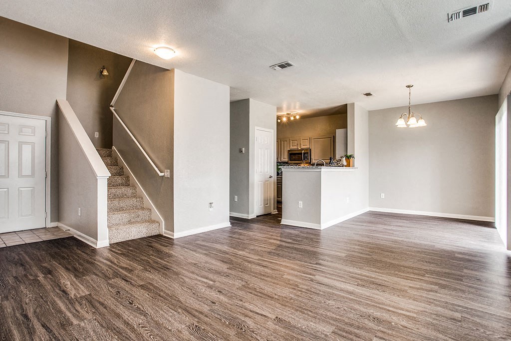 an empty living room with a staircase and a kitchen in the background