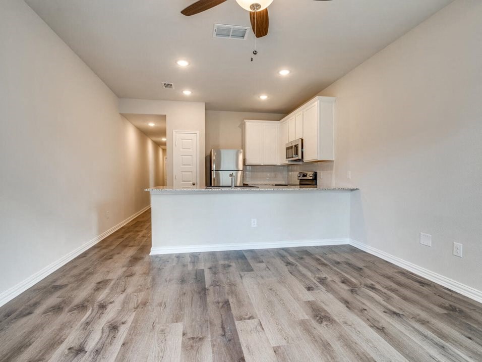 an empty living room with a kitchen in the background