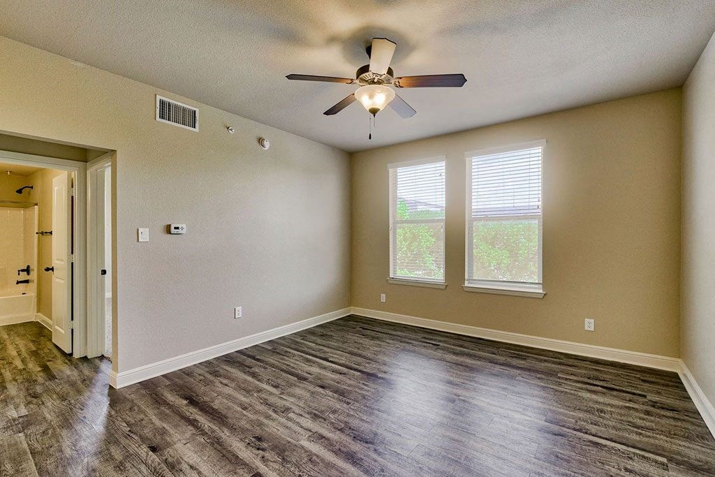 an empty bedroom with a ceiling fan and two windows