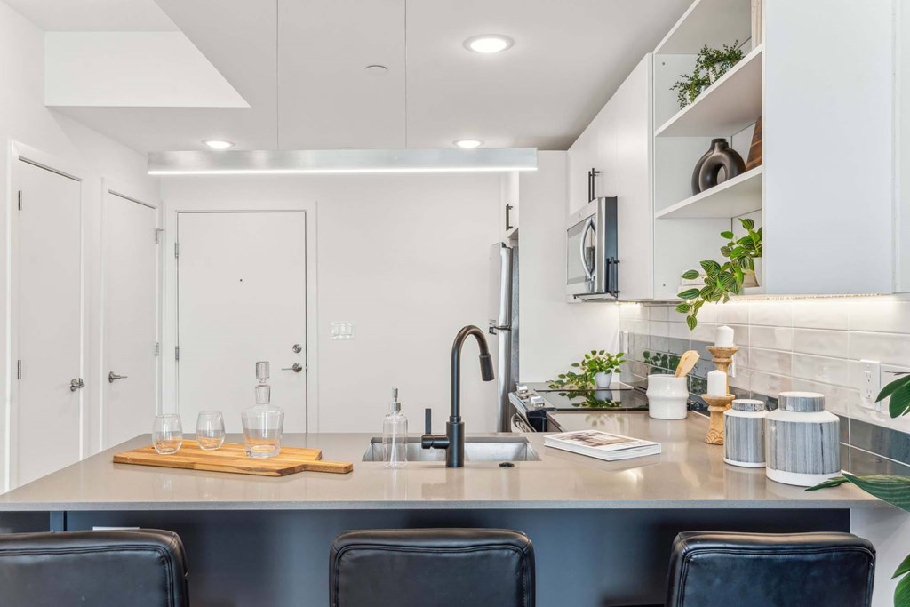 A modern kitchen with a stainless steel island and black chairs.