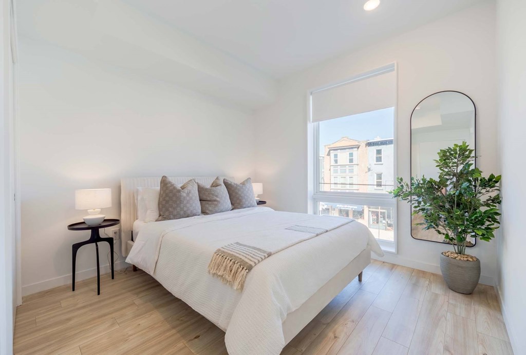 A bedroom with a large bed, a small table, and a potted plant.