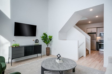 A living room with a grey coffee table and a black TV mounted on the wall.