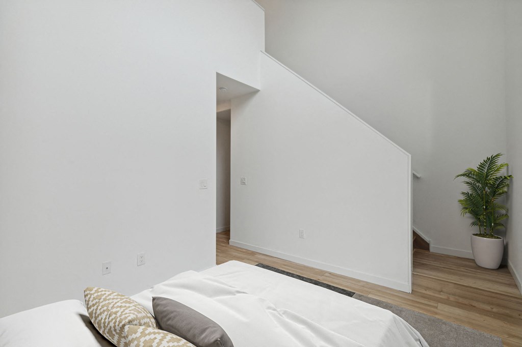 Minimalist bedroom featuring a double bed with light bedding, abstract artwork, and a stairway leading to an upper level, creating a sense of space and simplicity.
