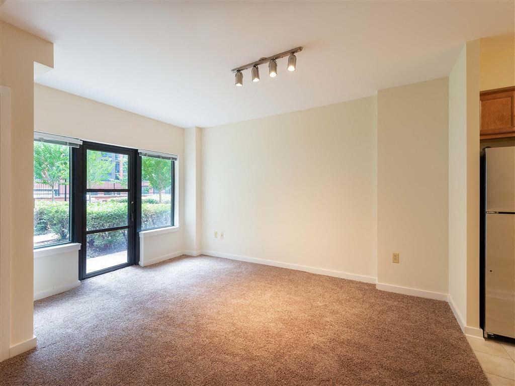 an empty living room with a refrigerator and a window